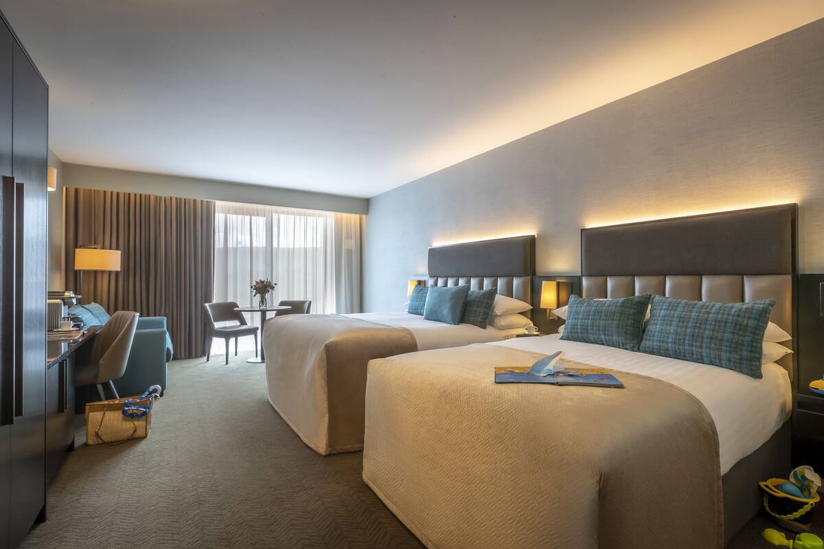 A hotel room with two beds, a desk, and a chair.