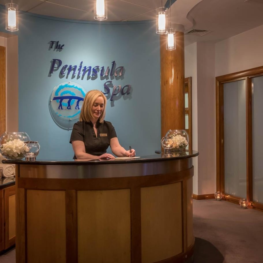 A reception desk at The Peninsula Spa with a blue wall, wooden paneling, and a logo.