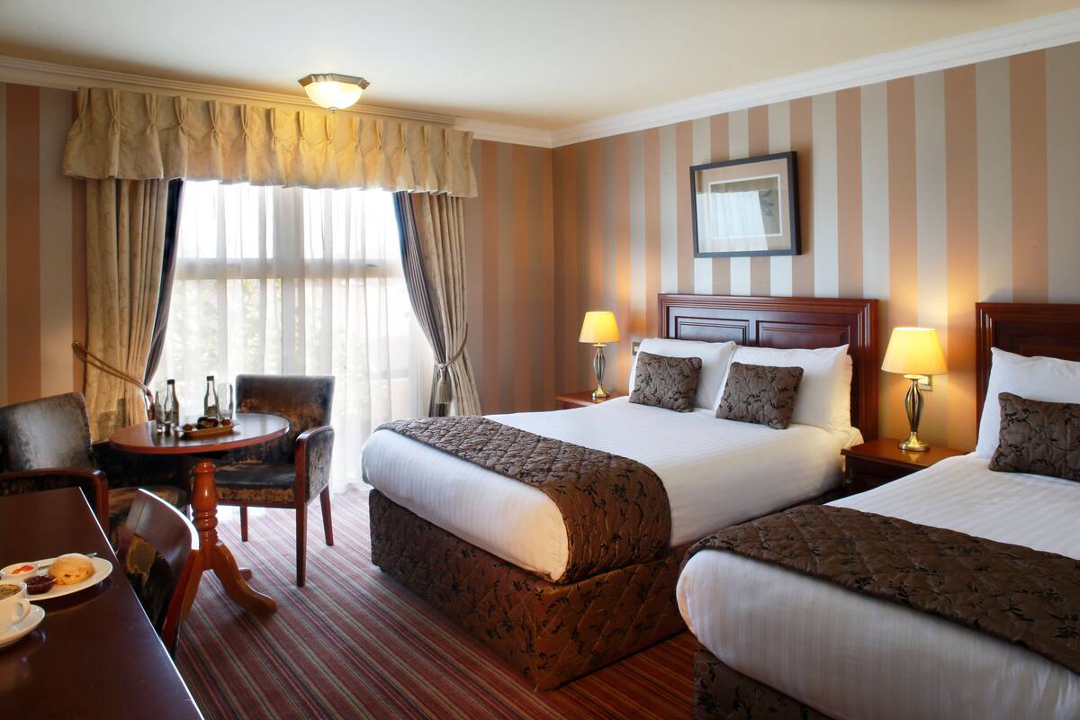 A hotel room with two beds, a dining table, and a small seating area.