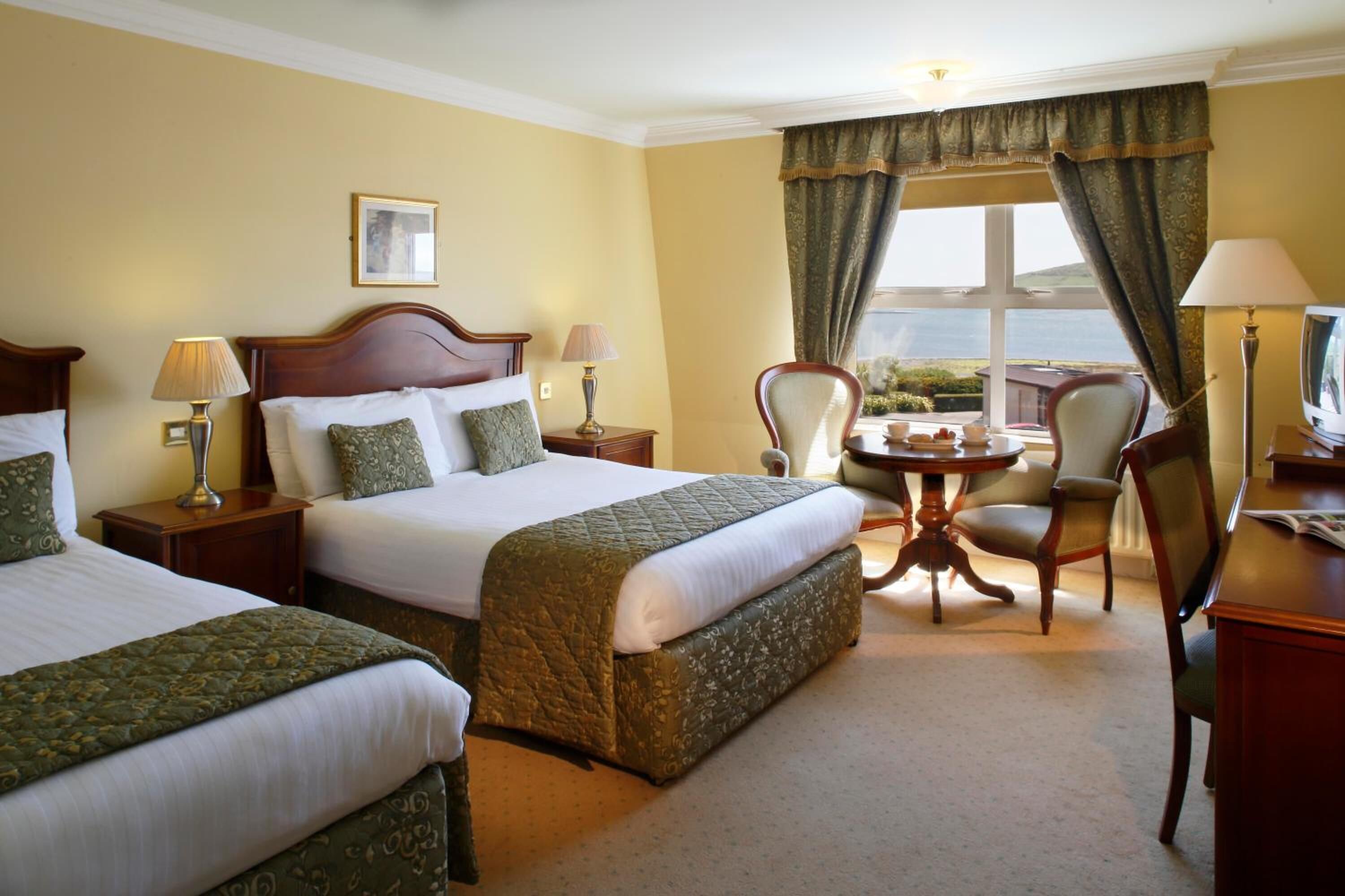 A hotel room with two beds, a desk, a chair, and a view of the outdoors.