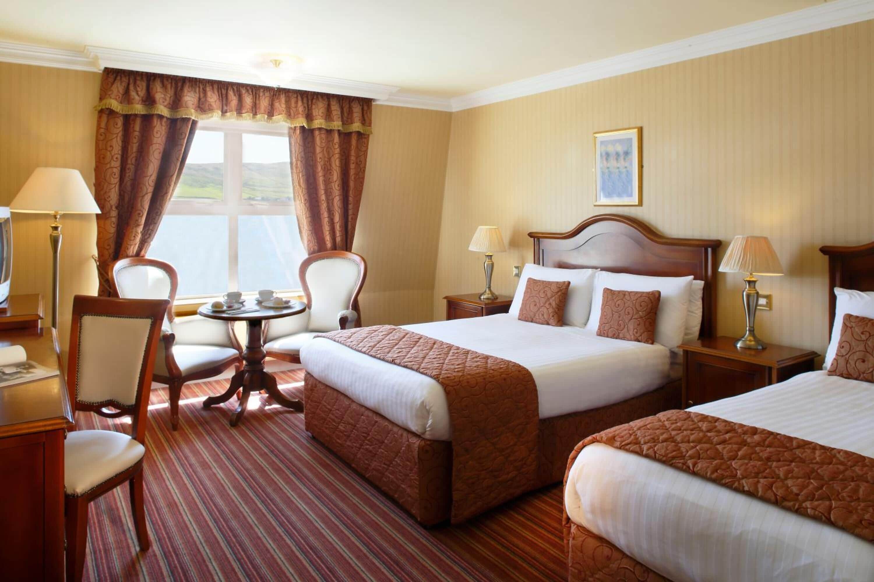 A hotel room with two beds, a round table, chairs, and a view of the outdoors.