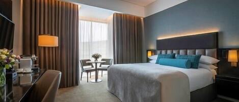 Una habitación de hotel con una cama grande, un escritorio con lámpara, una silla y una mesita con un jarrón de flores.