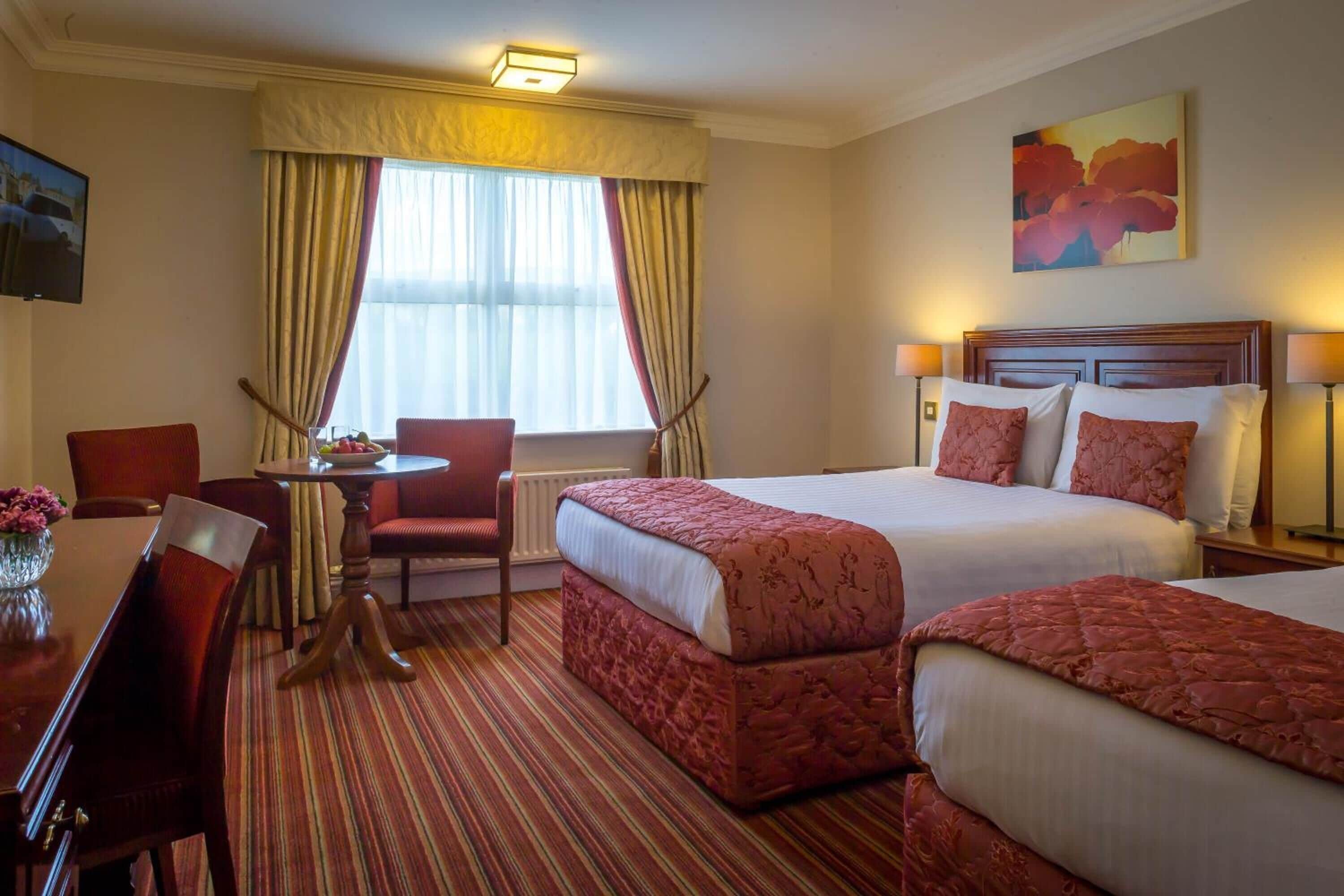 A hotel room with two beds, a dining table, a chair, and a TV.