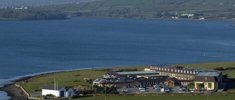 Un hôtel situé sur la côte, composé de plusieurs bâtiments, doté d’un parking et offrant une vue sur la mer et les collines.