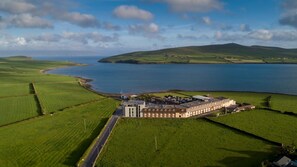 A large, rectangular building with a central courtyard, surrounded by green fields and a body of water.