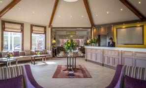 A spacious lobby with a high ceiling, a reception desk, seating area, and a view of the outdoors.