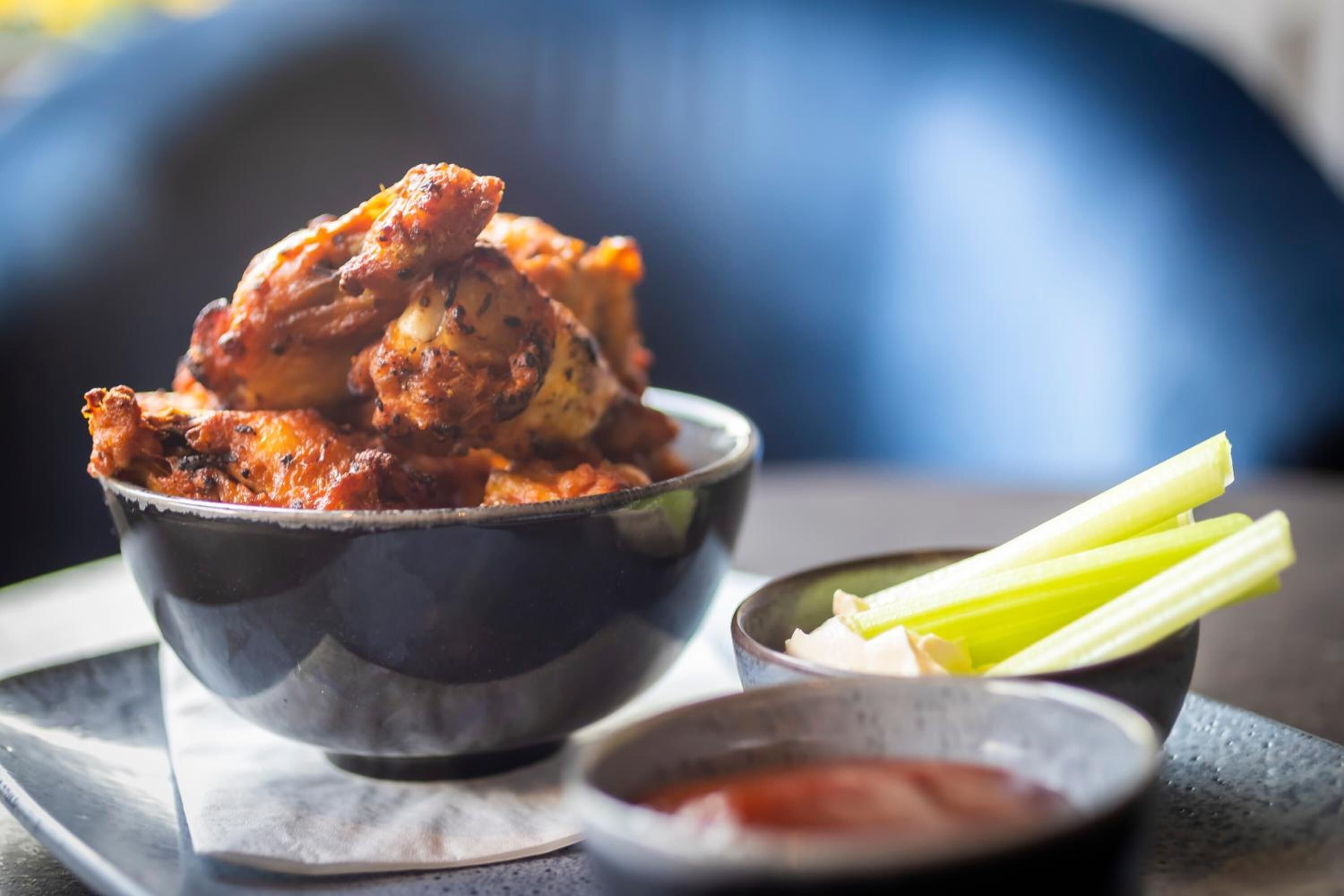 A bowl of chicken wings with celery sticks and a small bowl of sauce.