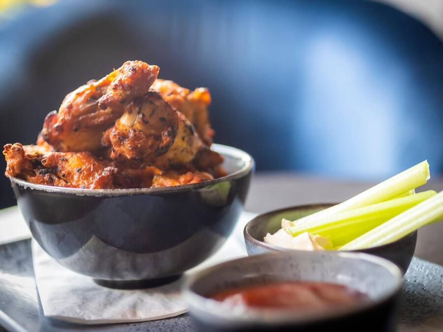 A bowl of chicken wings with celery sticks and a small bowl of sauce.
