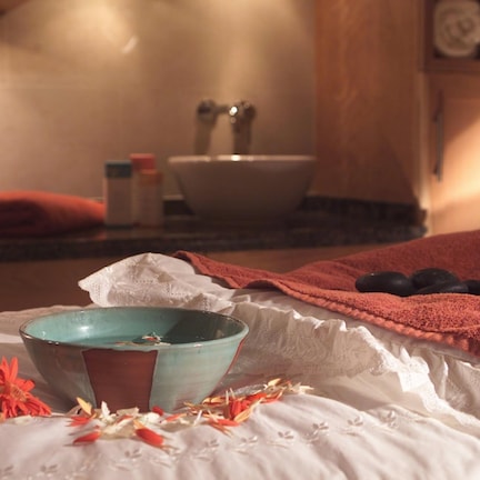 A bathroom with a sink, a towel, and a bowl on a bed.