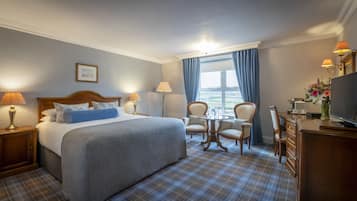 A hotel room with a bed, two chairs, a desk with a TV, a coffee maker, and a window with curtains.