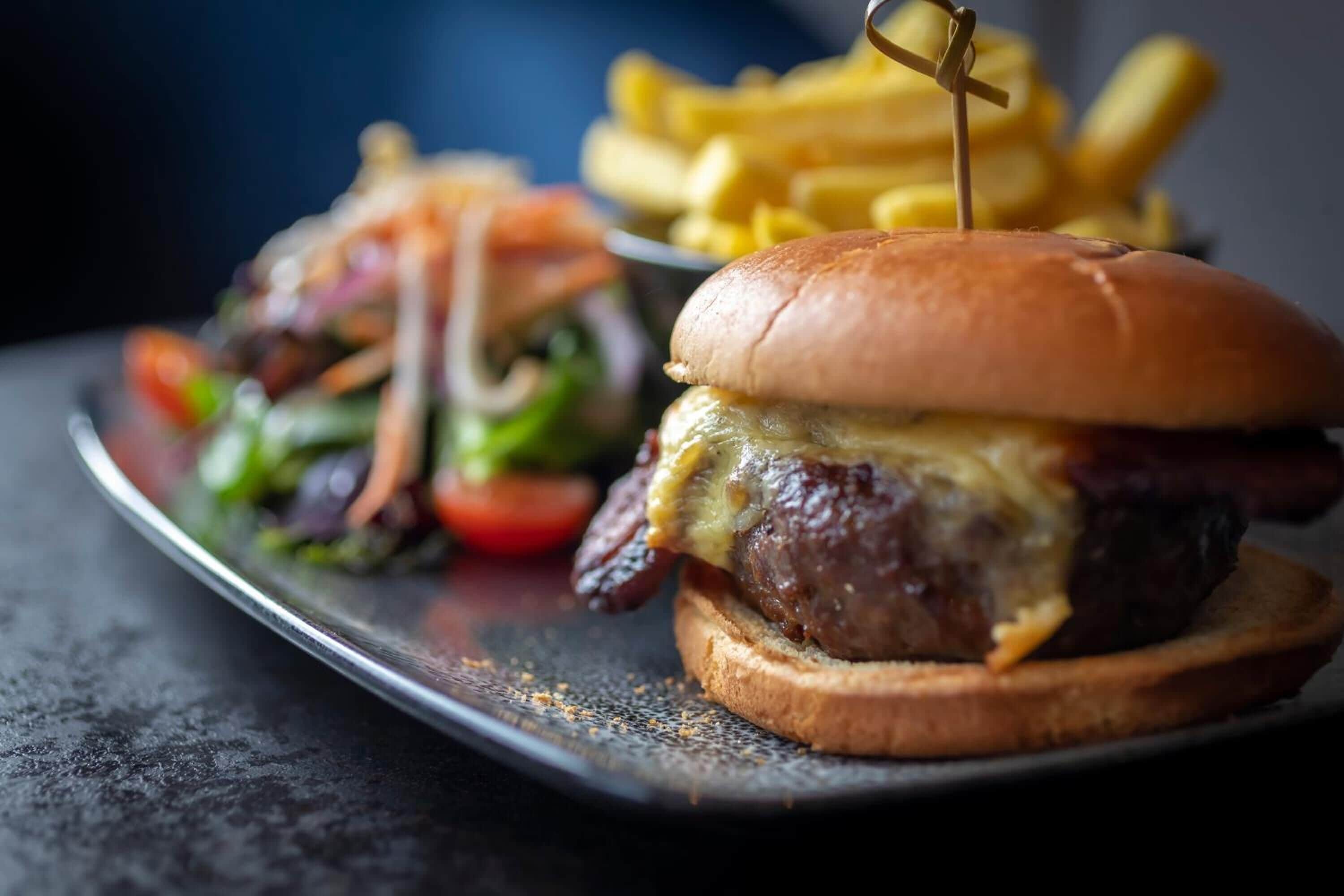 A burger with a toothpick on top, accompanied by a side of fries.