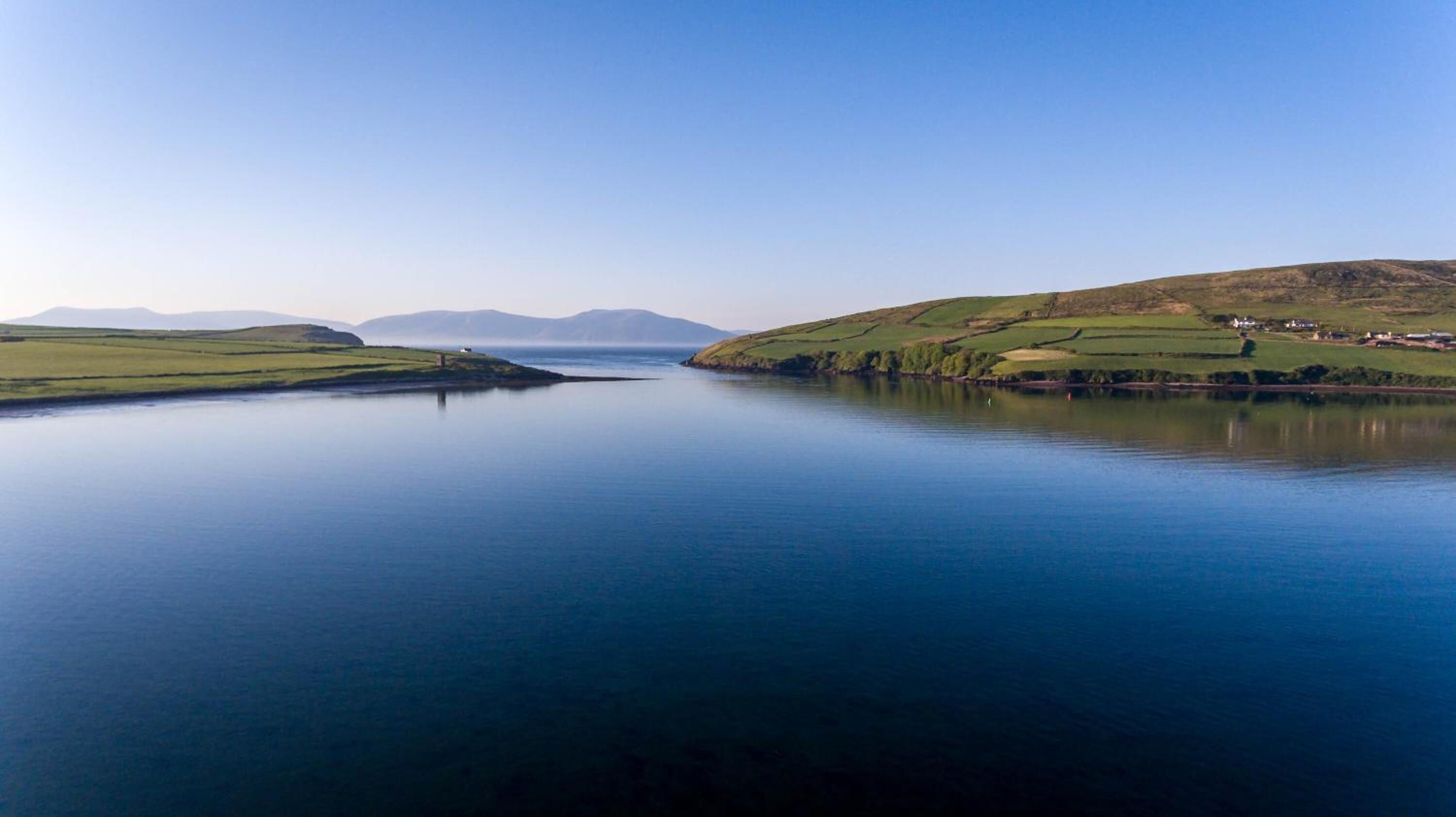 A tranquil lake surrounded by green hills and distant mountains.