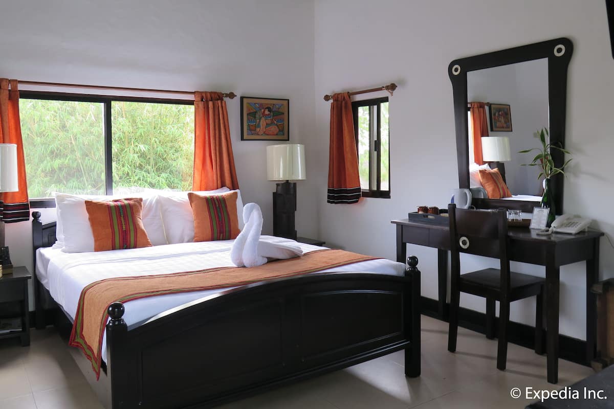 A hotel room with a bed, a desk, a chair, a mirror, and a window with curtains.