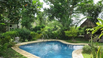Relax by the serene pool surrounded by lush greenery and a small waterfall feature.