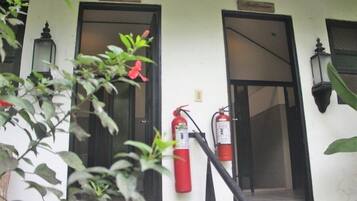 Ein Gebäudeeingang mit zwei an der Wand befestigten Feuerlöschern, einem Schild über der Tür und einem Blumentopf im Vordergrund.