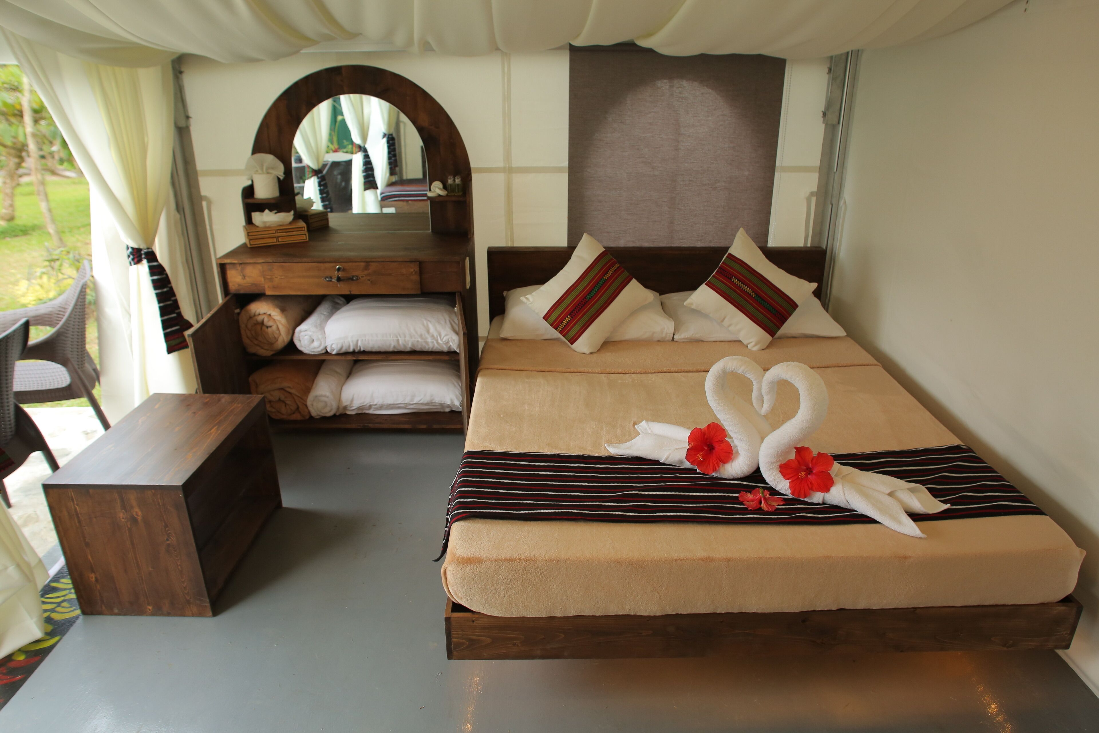 A neatly arranged bedroom with a bed, a wooden nightstand, a mirror, and a bench.