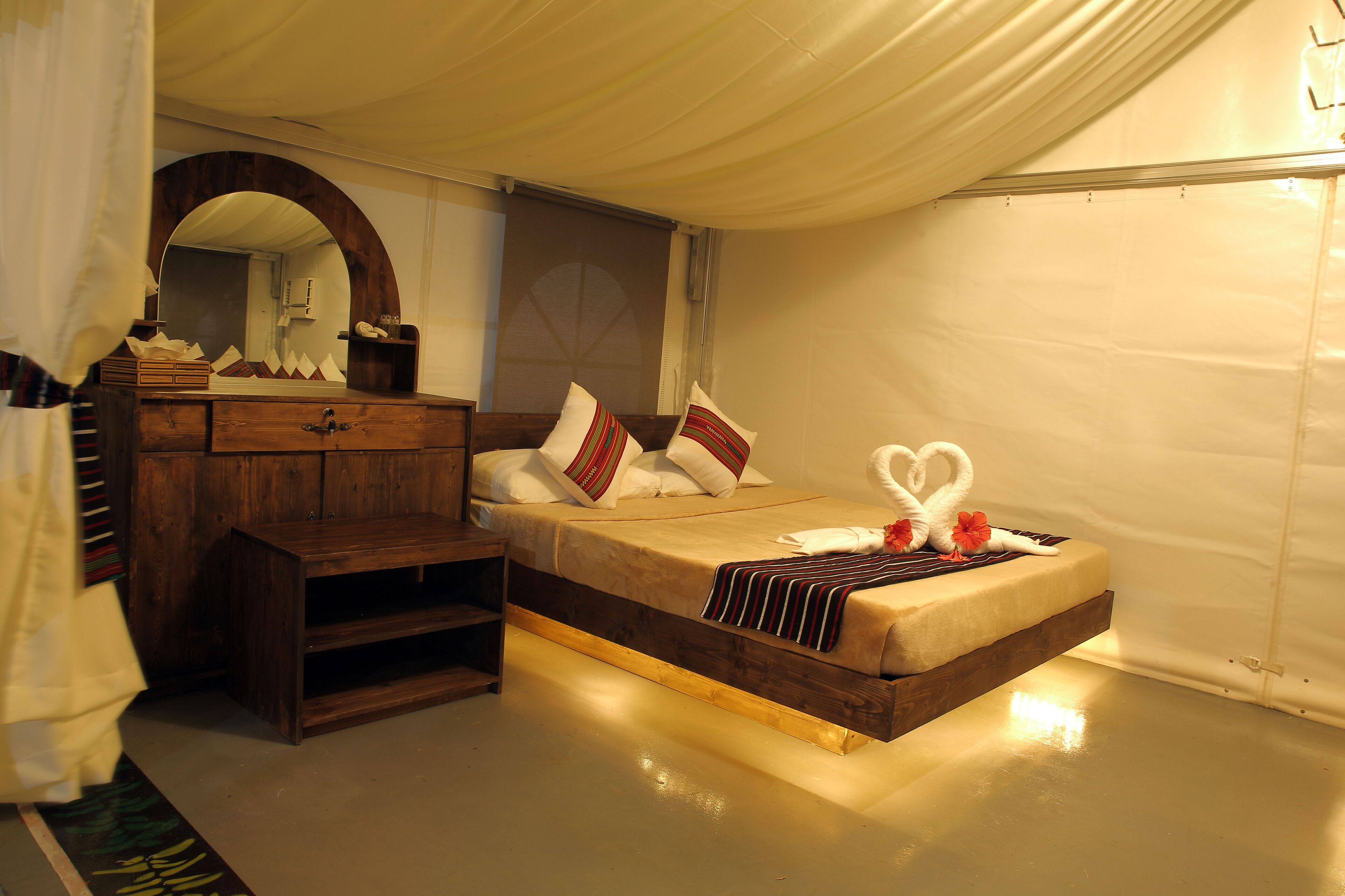 Un dormitorio con cama de madera, cómoda, espejo y un techo similar a una tienda de campaña.