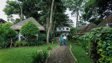 A pathway leading to a house surrounded by lush greenery and thatched-roof structures.