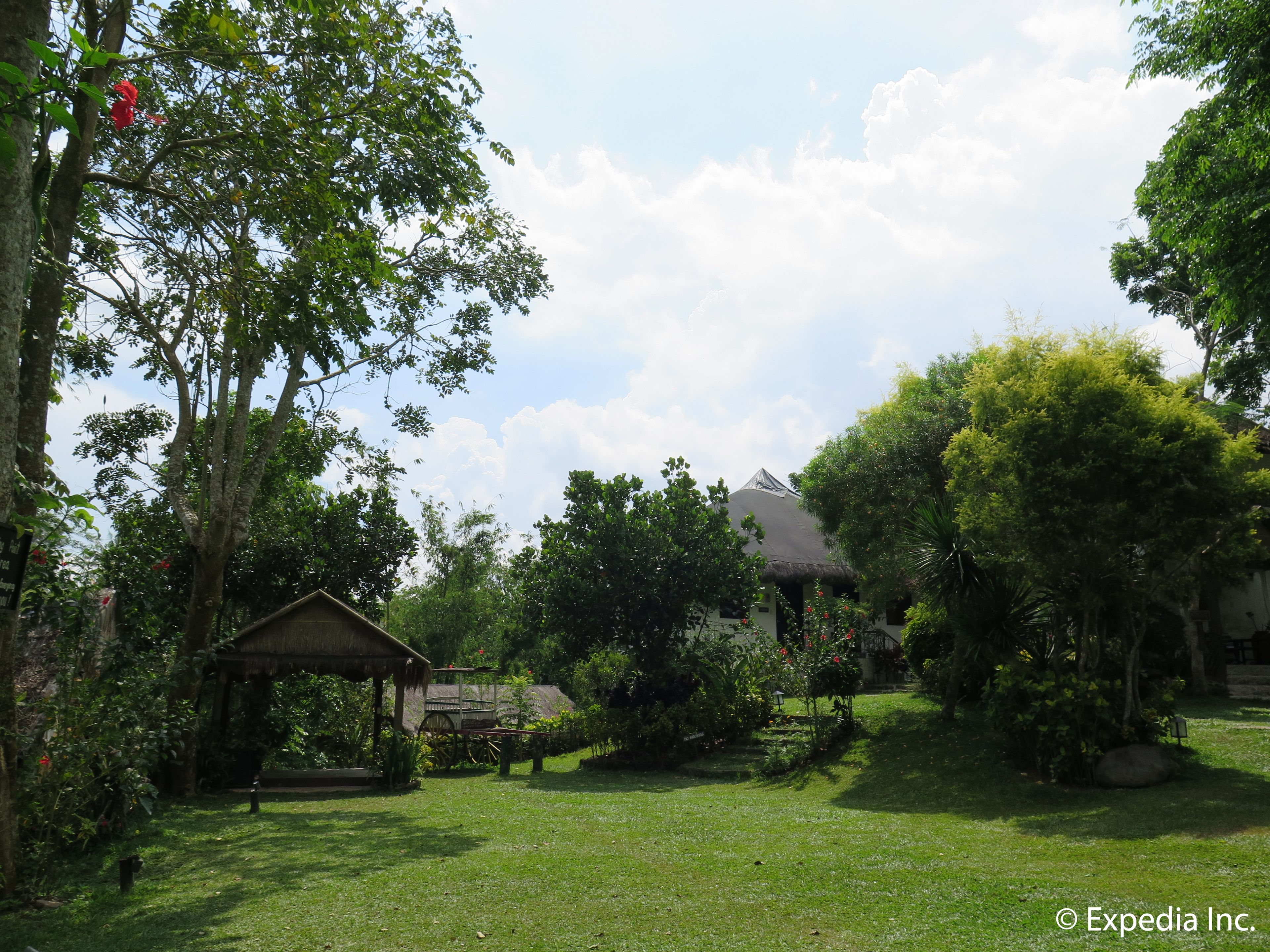 A lush garden with a gazebo, a thatched-roof house, and a variety of trees and plants.