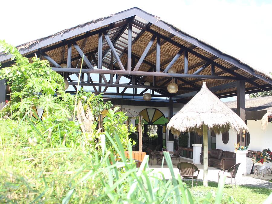 Un bâtiment doté d’un toit de chaume, d’un patio couvert avec des sièges extérieurs et offrant une vue sur la végétation environnante.