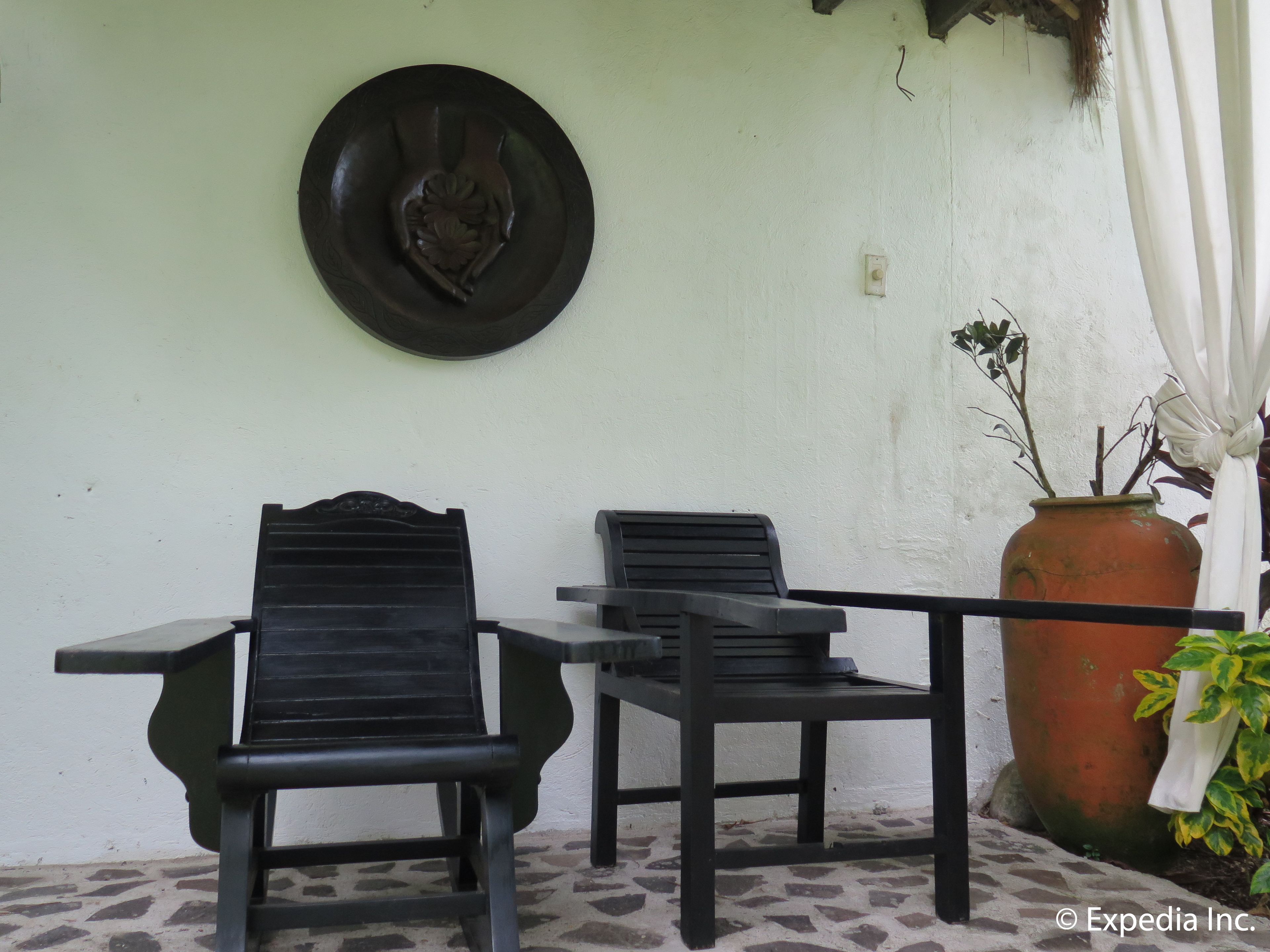 Two black lounge chairs and a table on a tiled patio with a white wall and a decorative plate above.