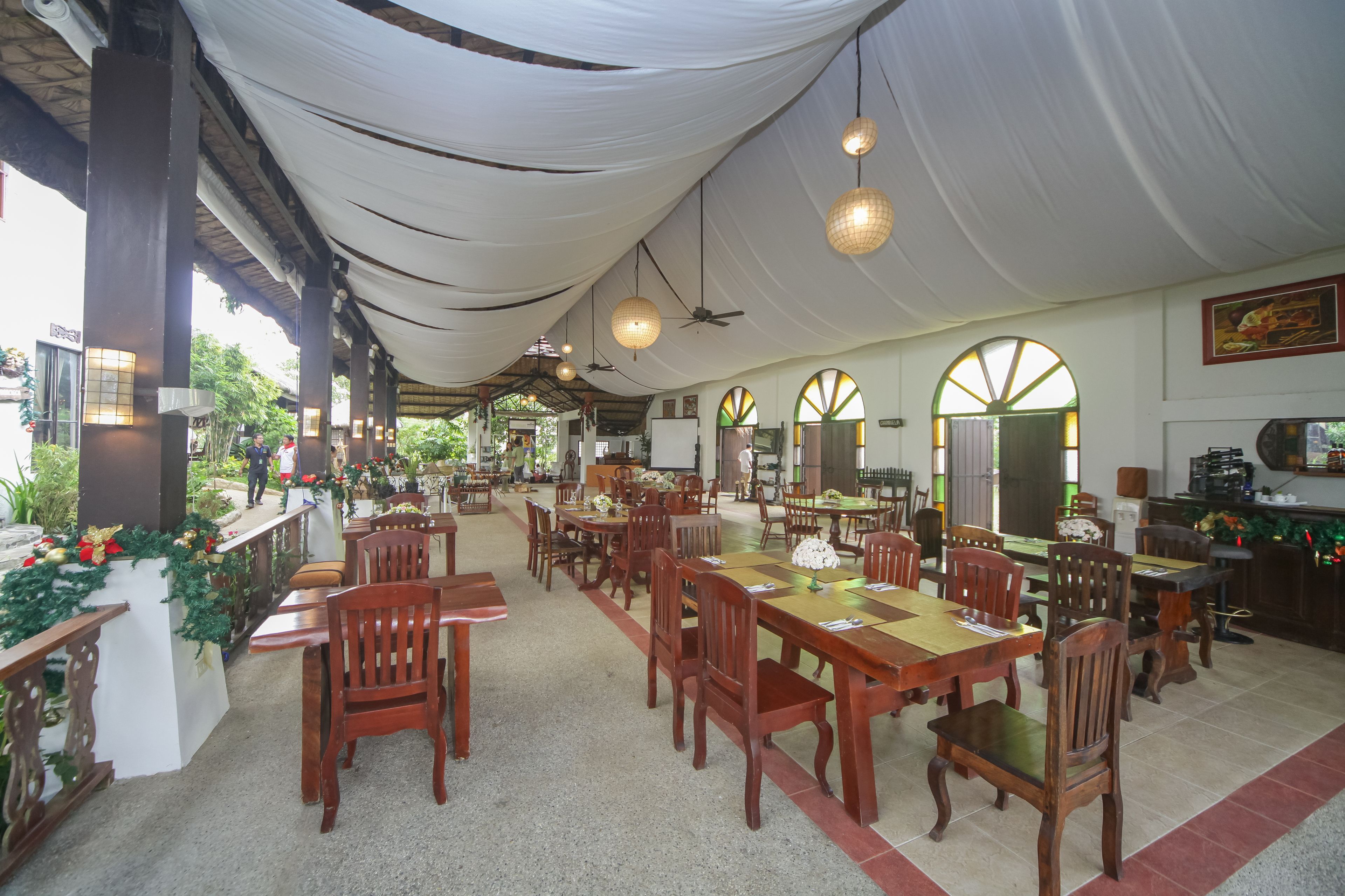A spacious indoor dining area with wooden tables and chairs, white draped ceilings, and large windows.