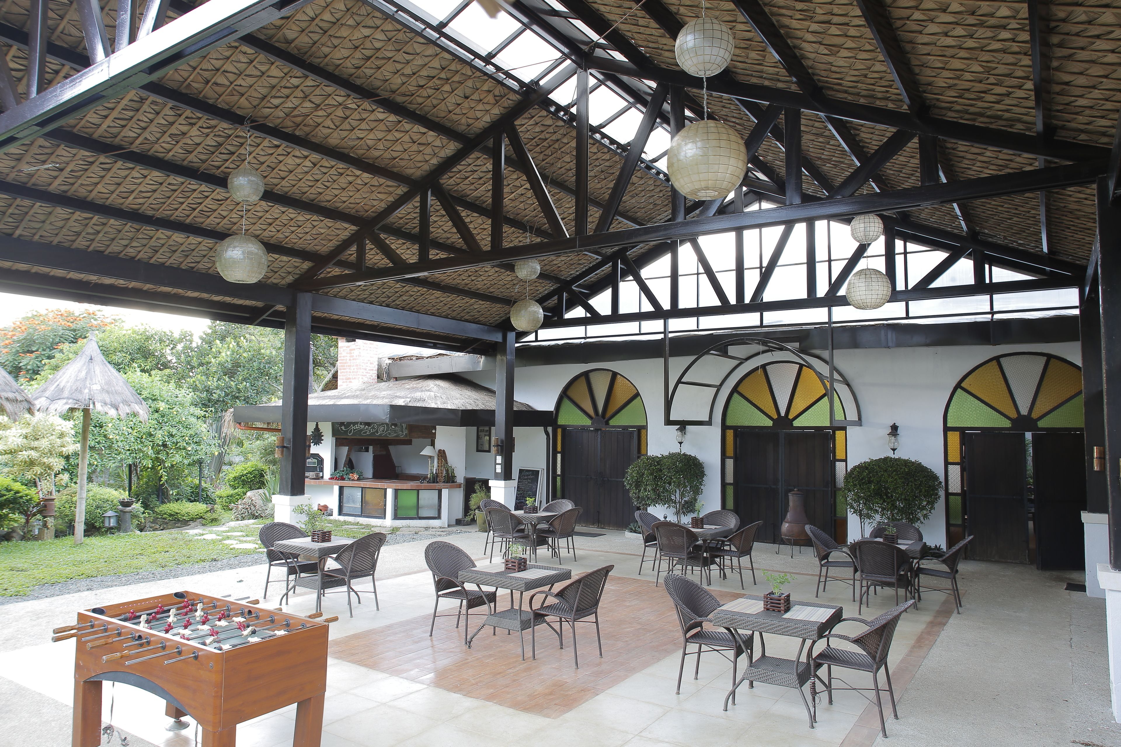 An outdoor patio area with tables and chairs, a foosball table, and a covered structure with a thatched roof.