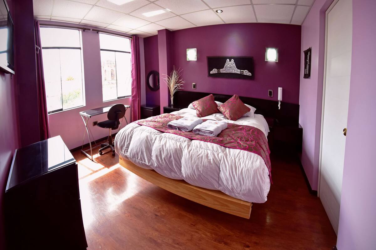 A bedroom with a large bed, a desk, and a window with curtains.