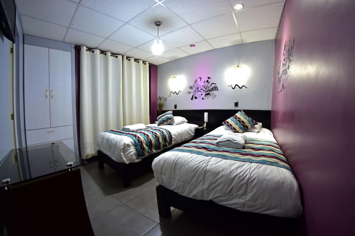A hotel room with two beds, a wardrobe, and a desk.