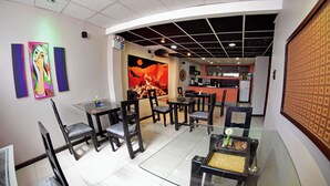 A dining area with glass tables and chairs, a kitchen in the background, and artwork on the walls. - Wifala Thematic Hotel (Cusco)