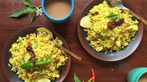 Two plates of yellow rice garnished with green chilies, a lime wedge, and a spoon. There is a blue cup and a brown bowl in the background. - Hotel Planet Plaza (Mumbai)