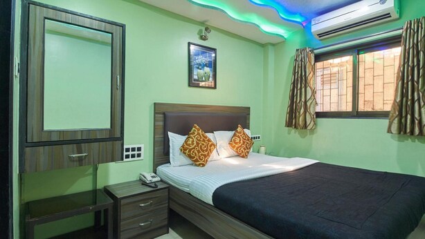 A bedroom with a bed, bedside table, and an air conditioning unit. - Hotel Planet Plaza (Mumbai)