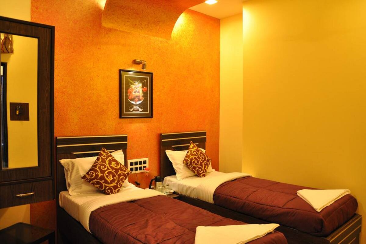A hotel room with two beds, each with a brown quilt and patterned pillows. There is a framed picture on the wall above the beds.
