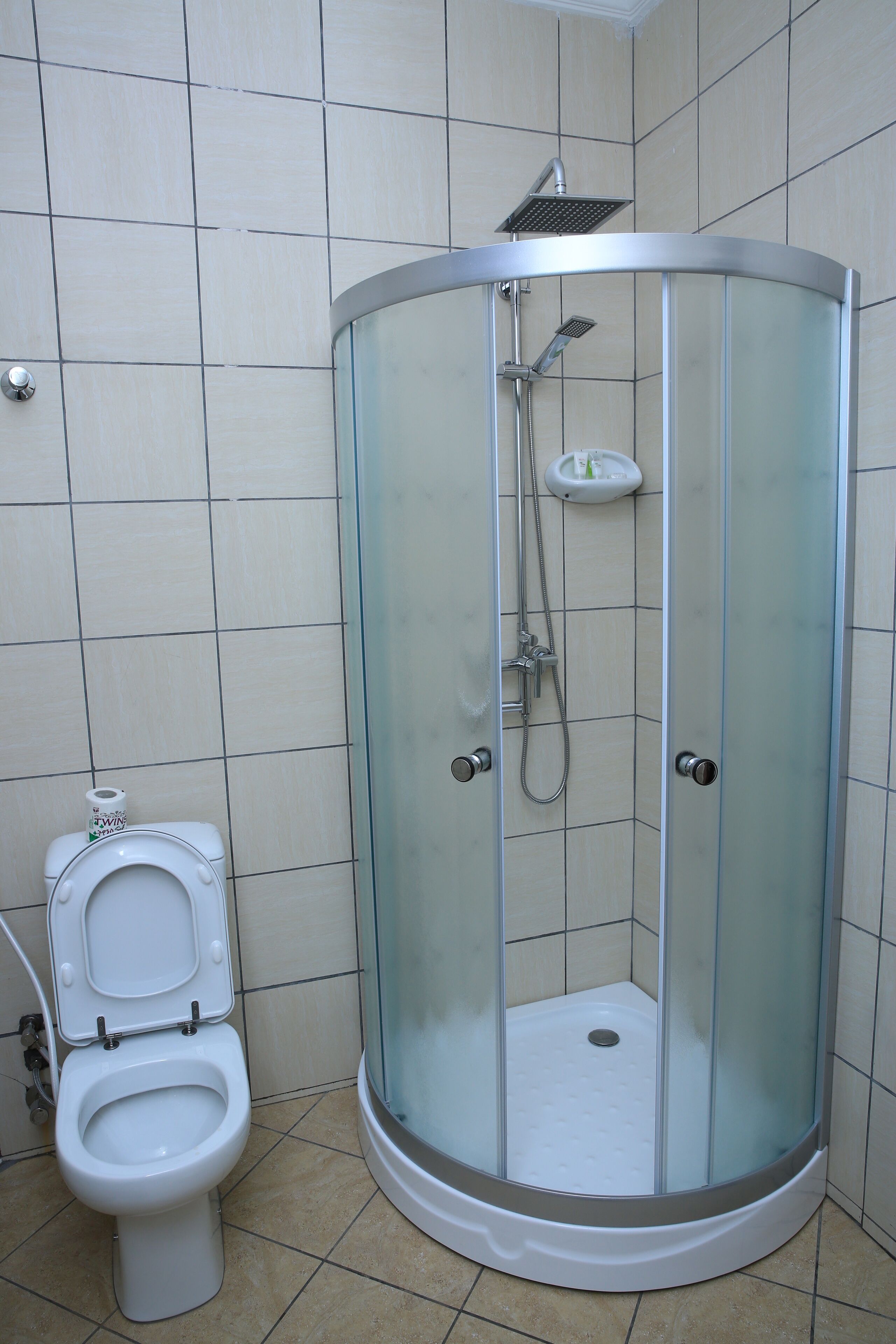 A bathroom with a glass-enclosed shower, a toilet, and tiled walls.