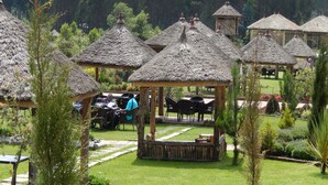 A series of thatched-roof structures, likely serving as outdoor seating areas, surrounded by well-maintained gardens and a backdrop of dense forest. - Yaya Africa Athletics Village (Sululta)