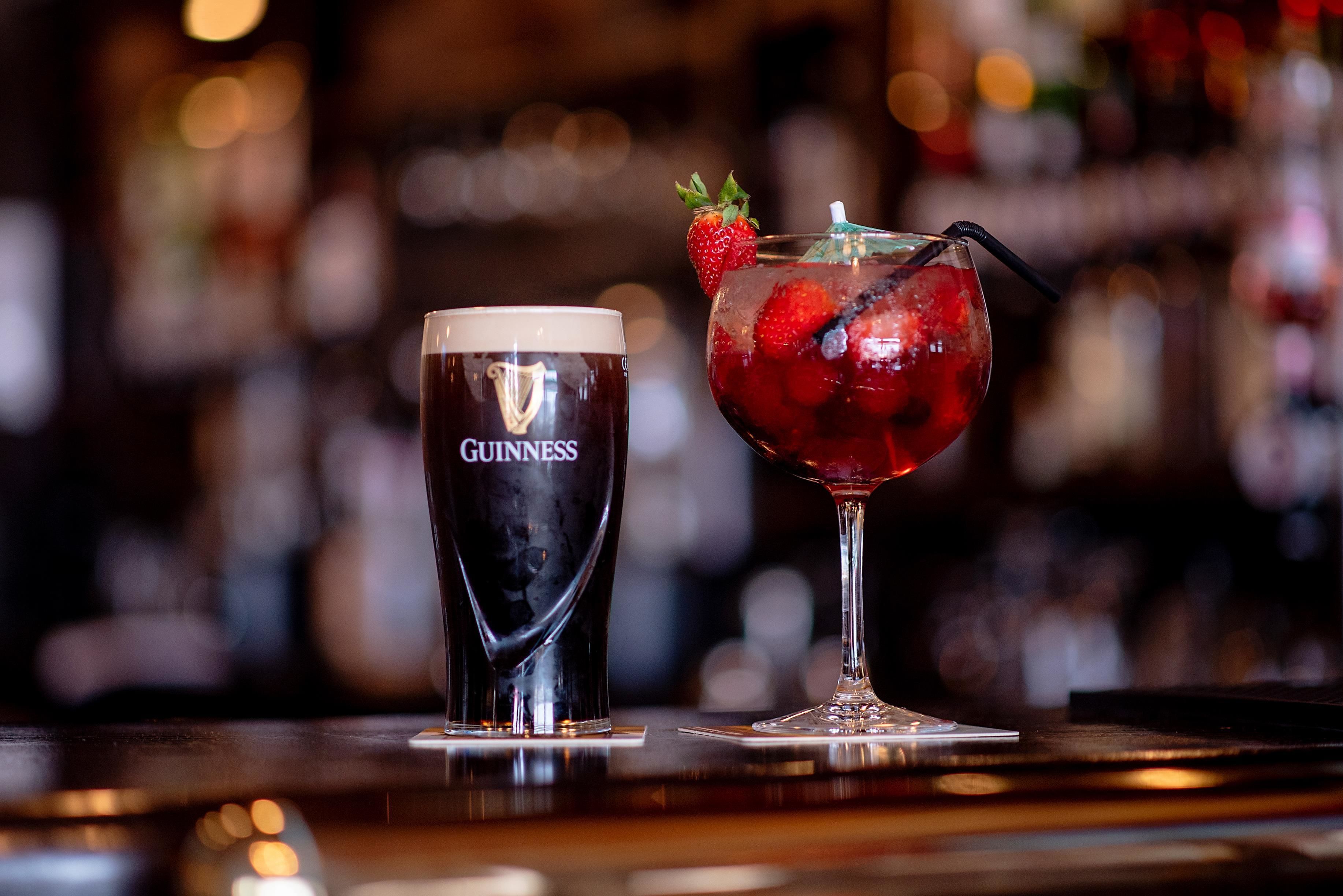 Una cerveza Guinness y un cóctel con fresas sobre una barra.