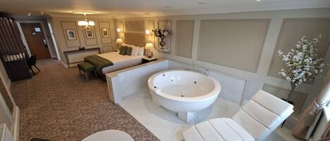 A modern hotel room with a large bathtub, a sofa, a dining table, and a separate seating area.