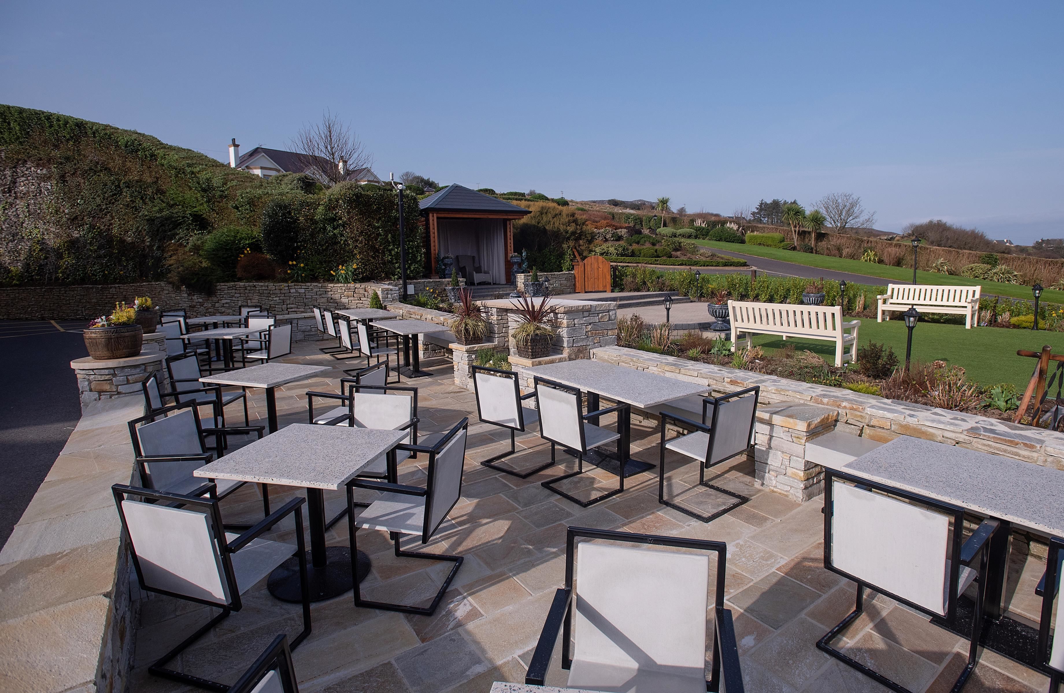 An outdoor patio with stone tables and chairs, a wooden gazebo, and a bench.
