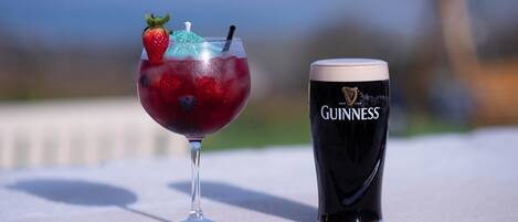 Un vaso de bebida roja con una fresa y un paraguas azul sobre una mesa. Junto a él, un vaso de Guinness.
