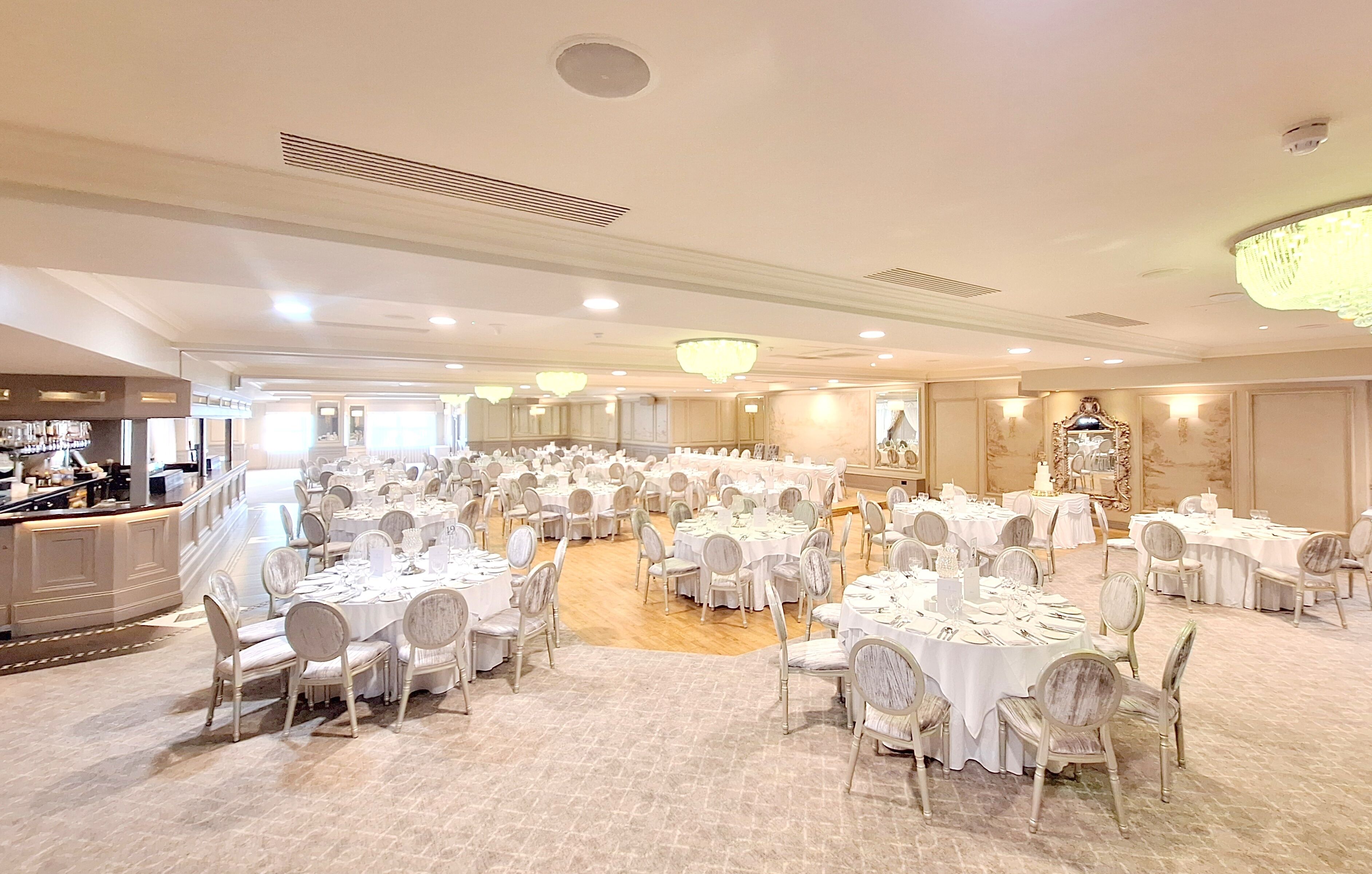 Un salón de banquetes con mesas redondas y sillas, una zona de bar y un candelabro.