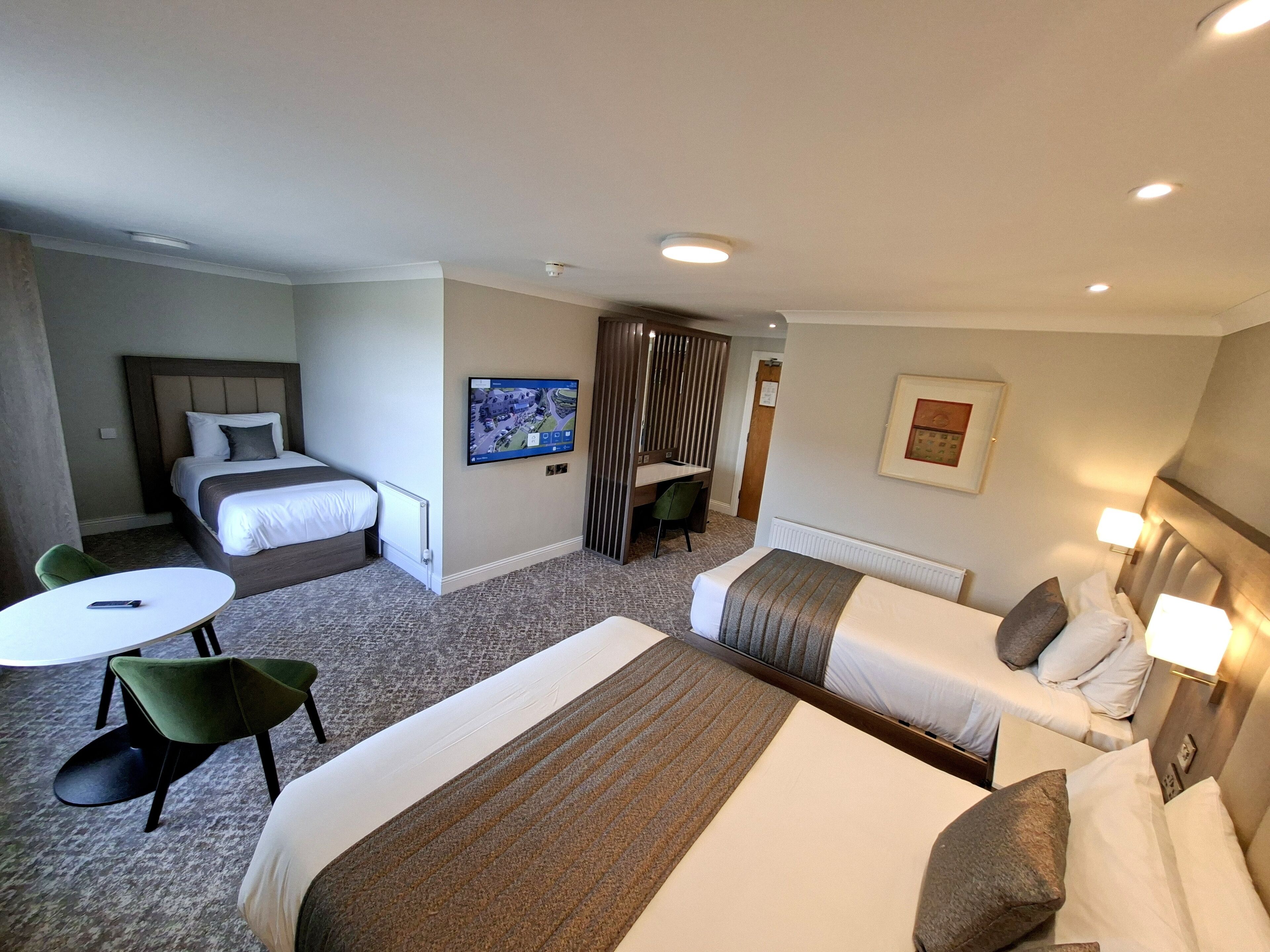 A hotel room with two beds, a desk, a chair, a TV, and a framed picture on the wall.