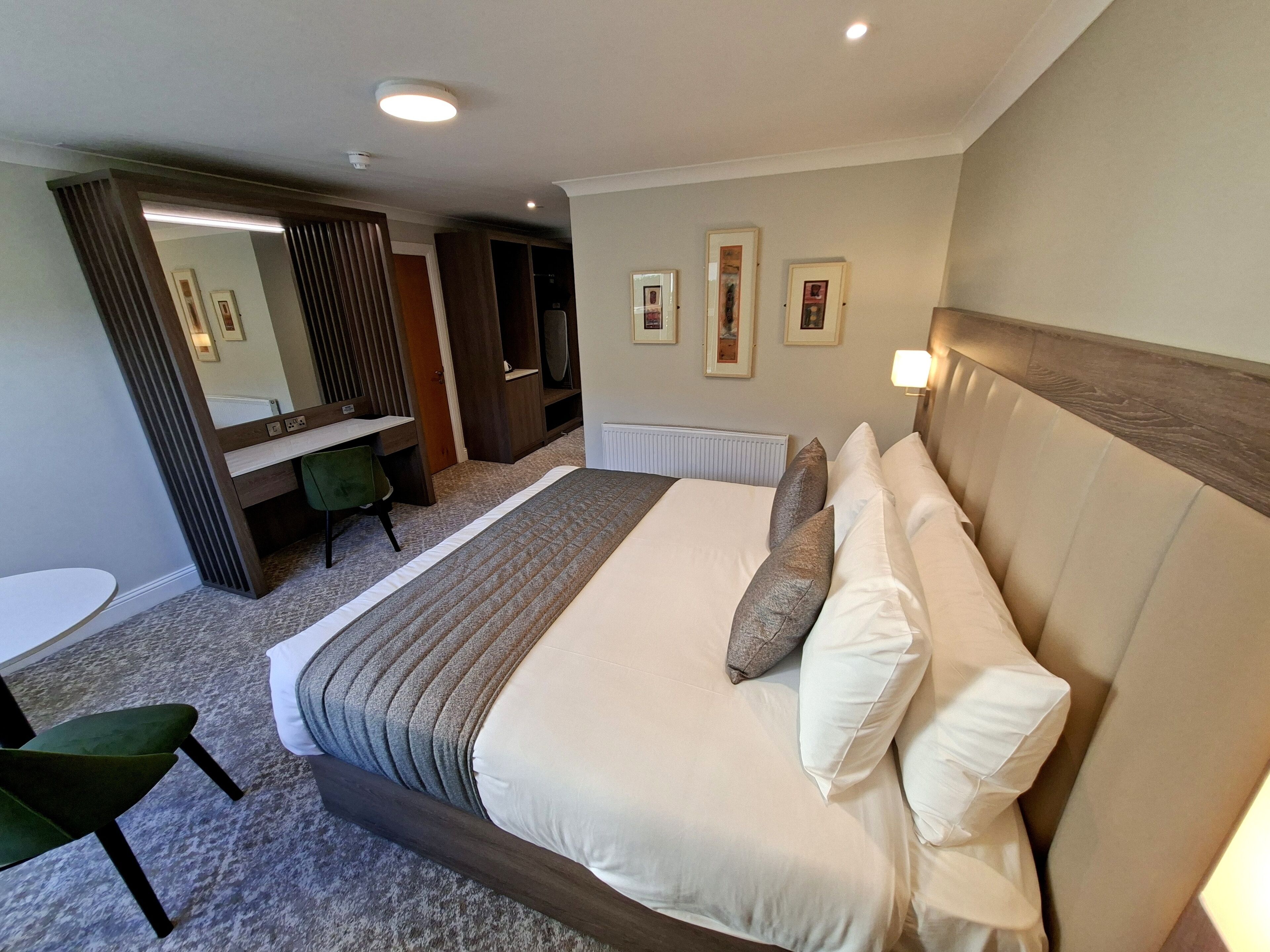 A hotel room with a large bed, a desk, a chair, and a mirror.