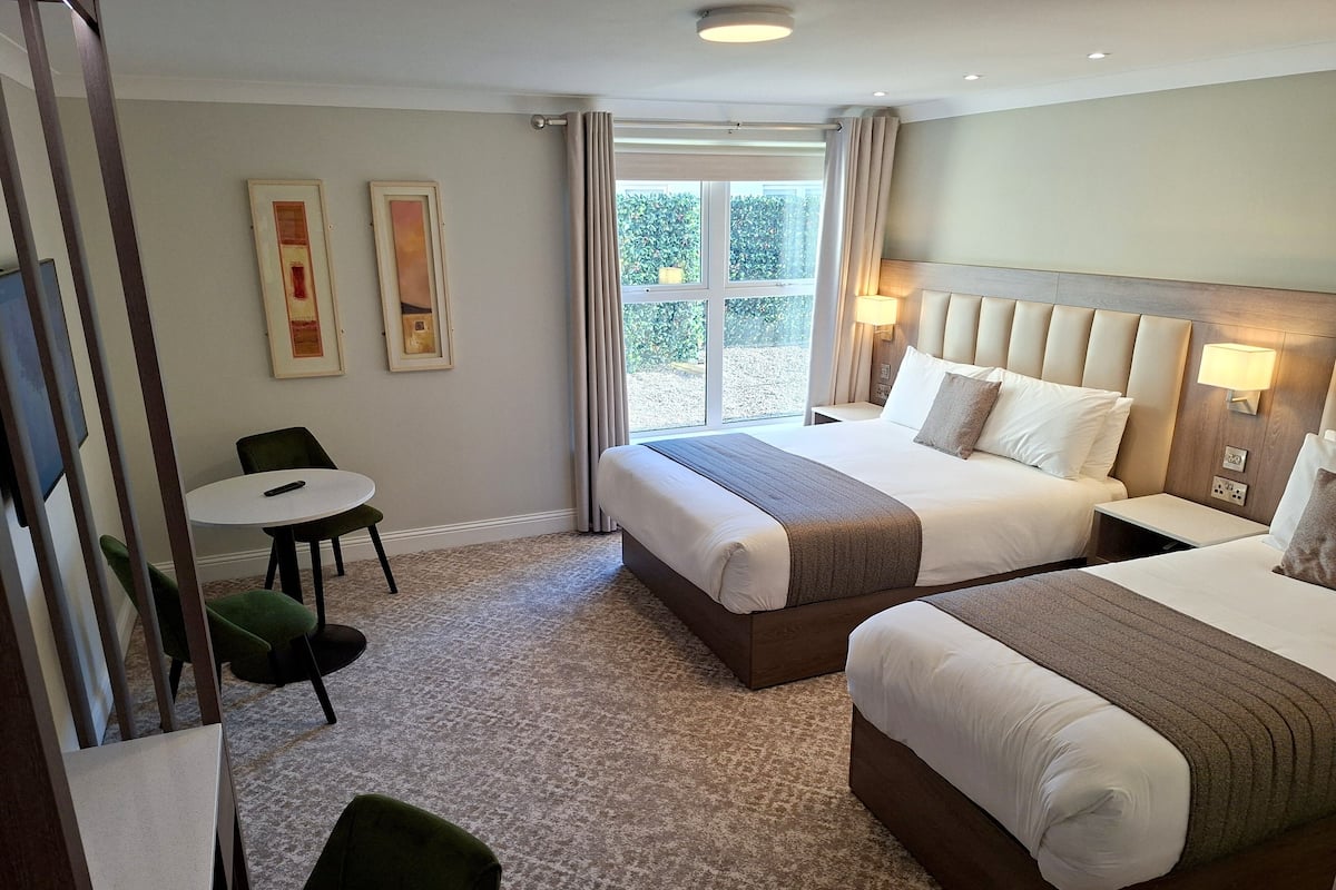 Une chambre d’hôtel avec deux lits, une petite table avec une chaise et une fenêtre avec des rideaux.