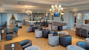 A spacious lobby with a bar area, seating arrangements, and a television screen displaying a welcome message.