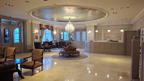 A spacious lobby with a high ceiling, elegant chandeliers, and a polished marble floor.