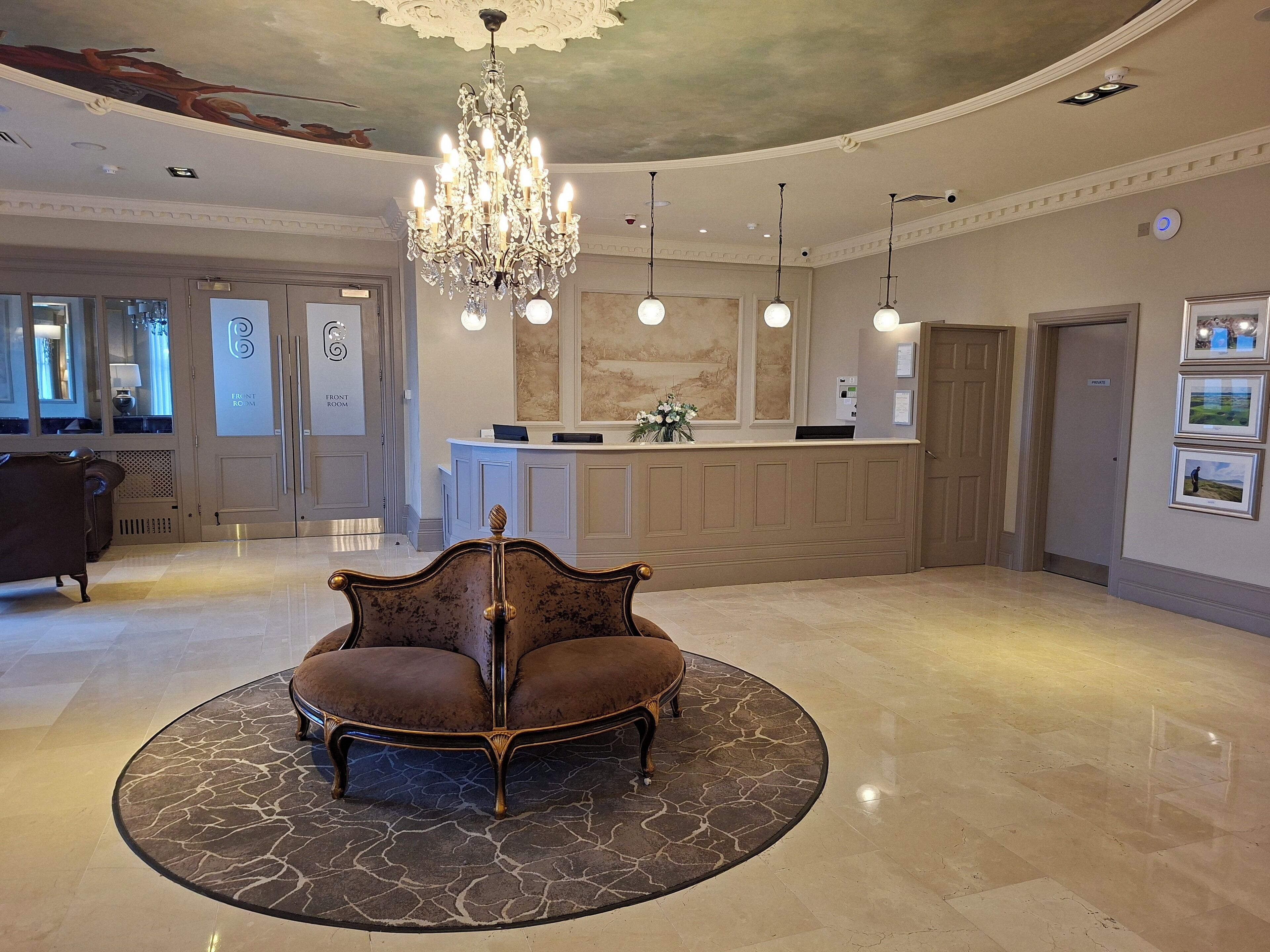 A lobby with a grand chandelier, a reception desk, and a seating area with a patterned rug.