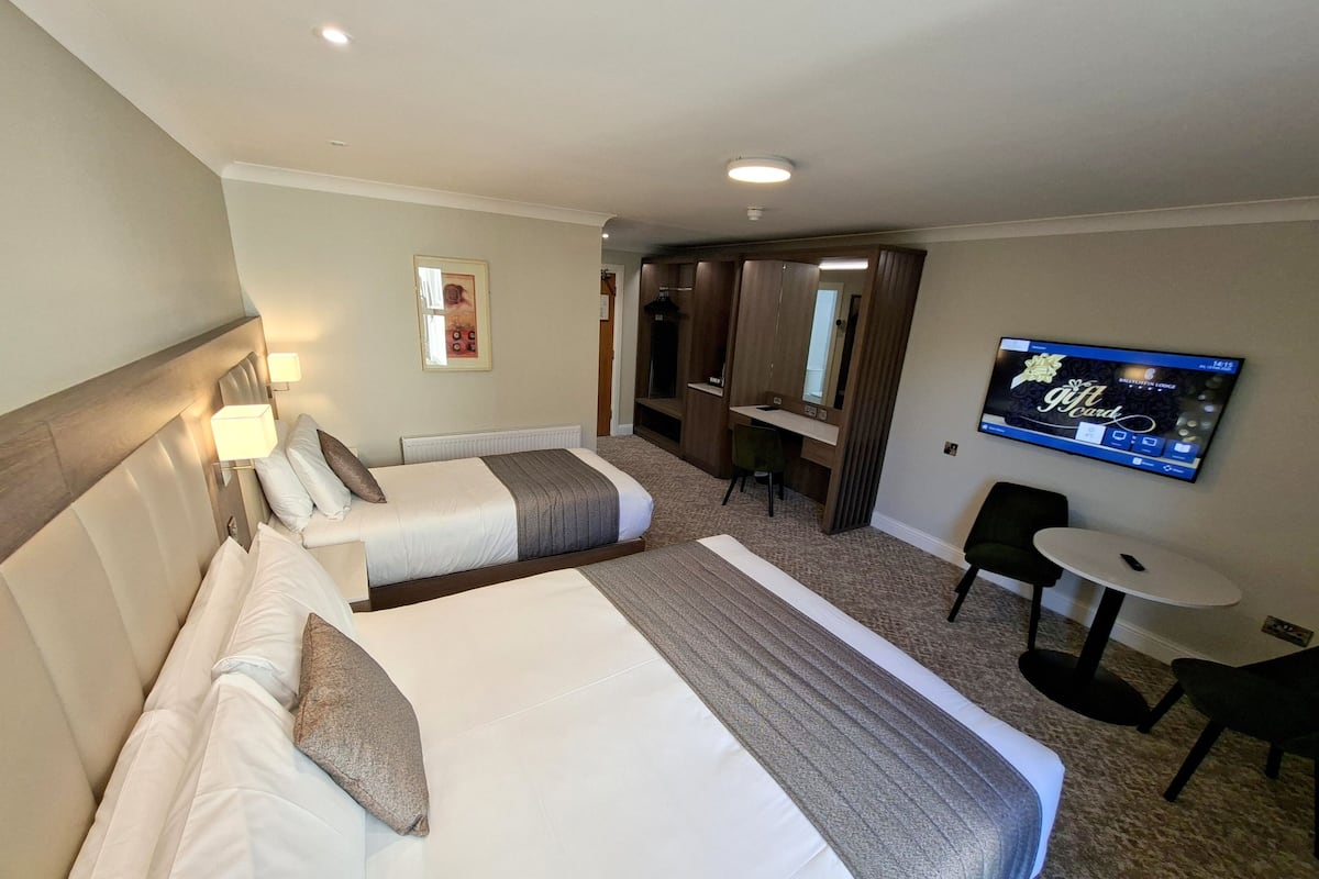 Une chambre d’hôtel avec deux lits, un bureau, une chaise, une télévision et une petite table.