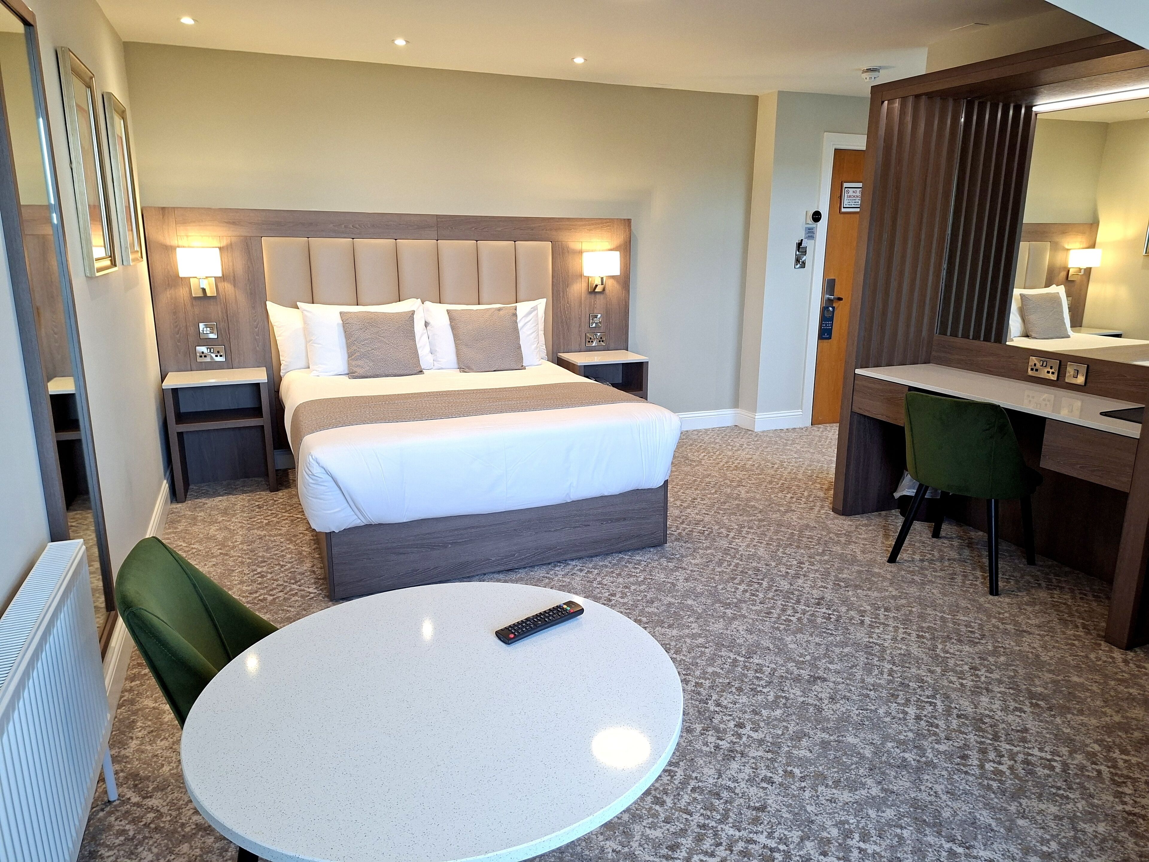 Una habitación de hotel con cama, lámparas de noche, un escritorio, una silla y una mesa redonda.