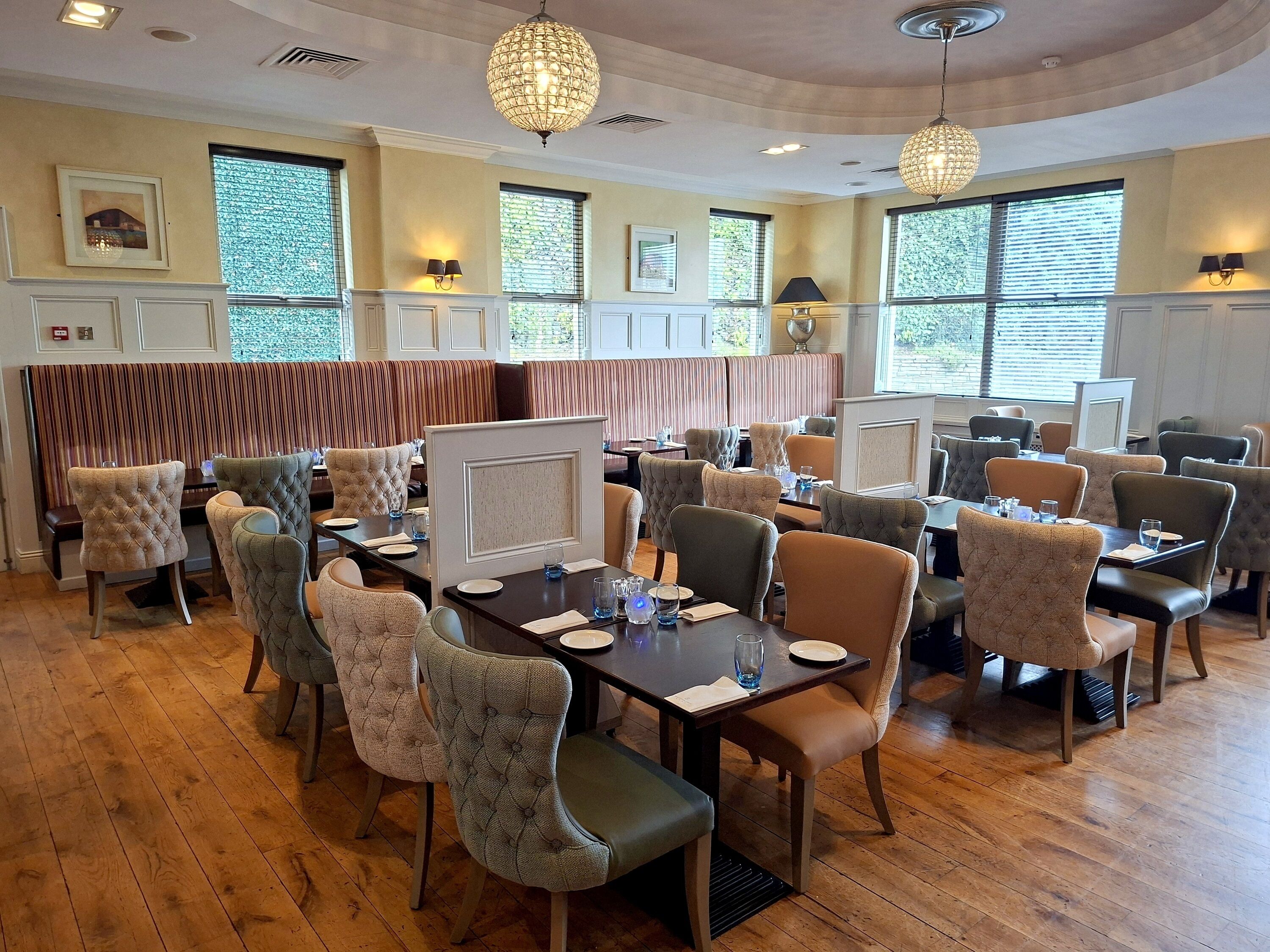 A dining area with booths and tables, wooden flooring, and pendant lighting.
