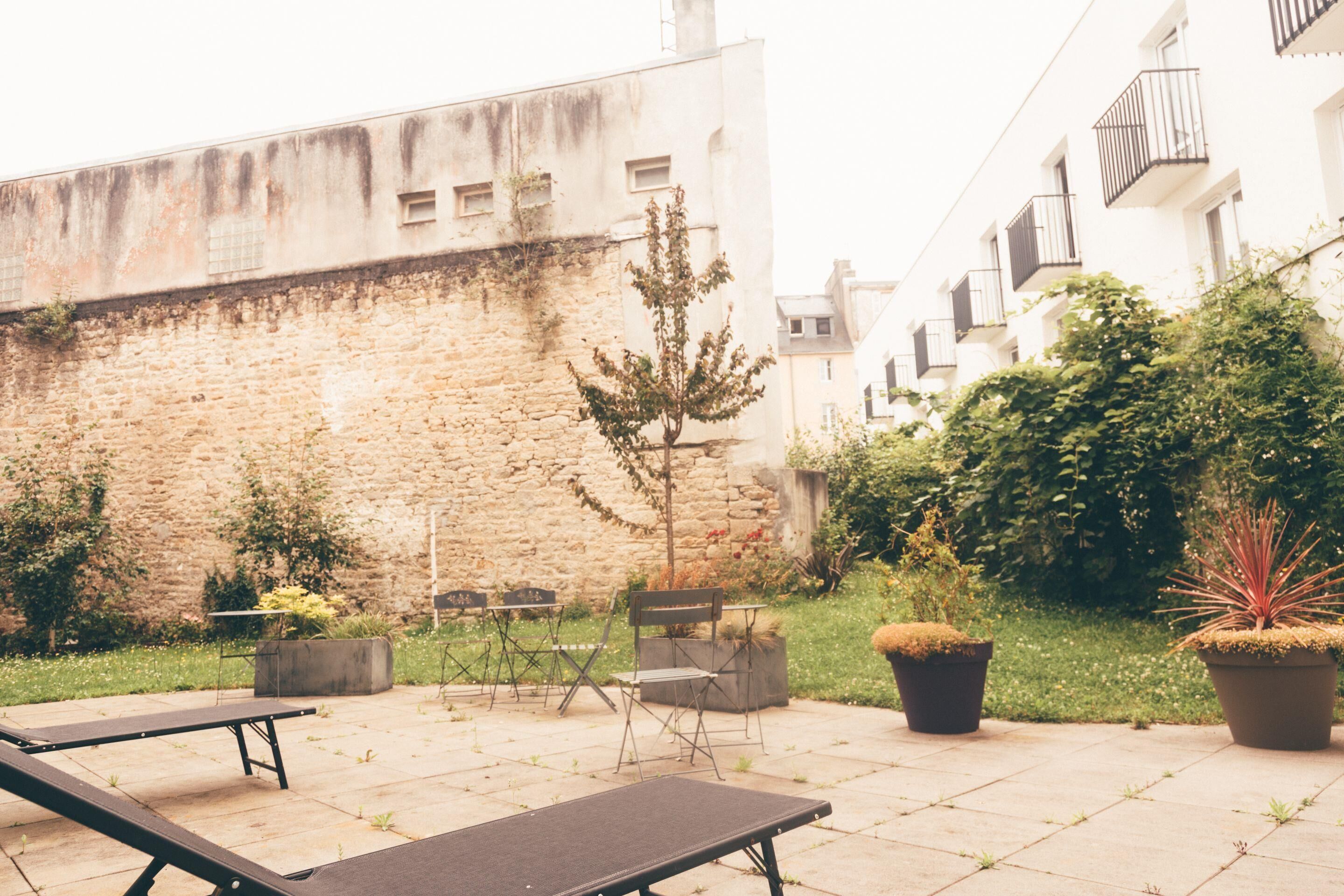 An outdoor patio with a stone wall, a small tree, potted plants, and outdoor furniture.